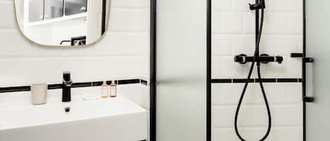 Une salle de bain moderne avec un lavabo blanc, un miroir, une douche équipée d’un pommeau de douche à main et un porte-serviettes avec des serviettes.
