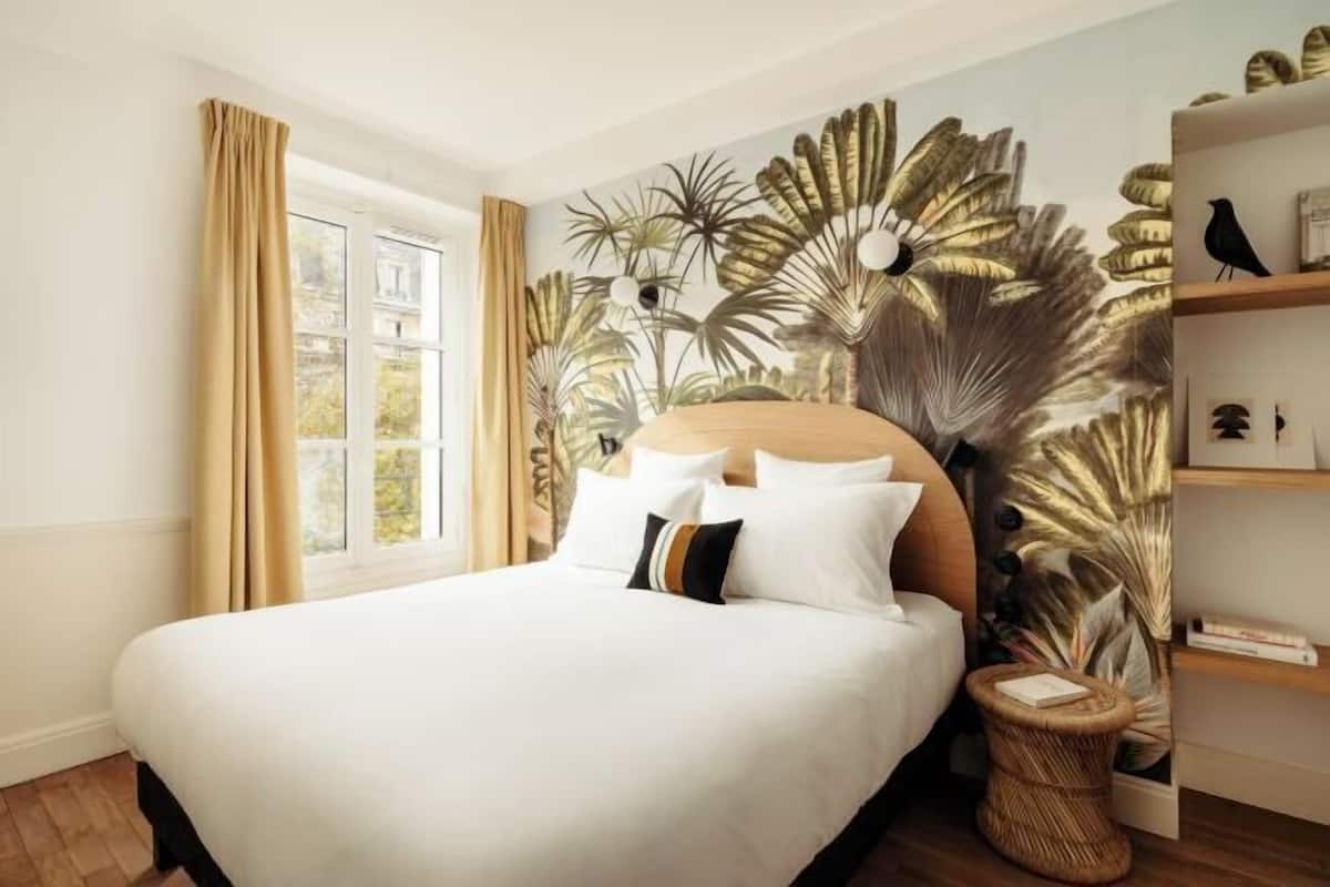 Ein ordentlich eingerichtetes Schlafzimmer mit einem großen Bett, einem Fenster mit Vorhängen, einer Wandmalerei und einem kleinen Nachttisch.