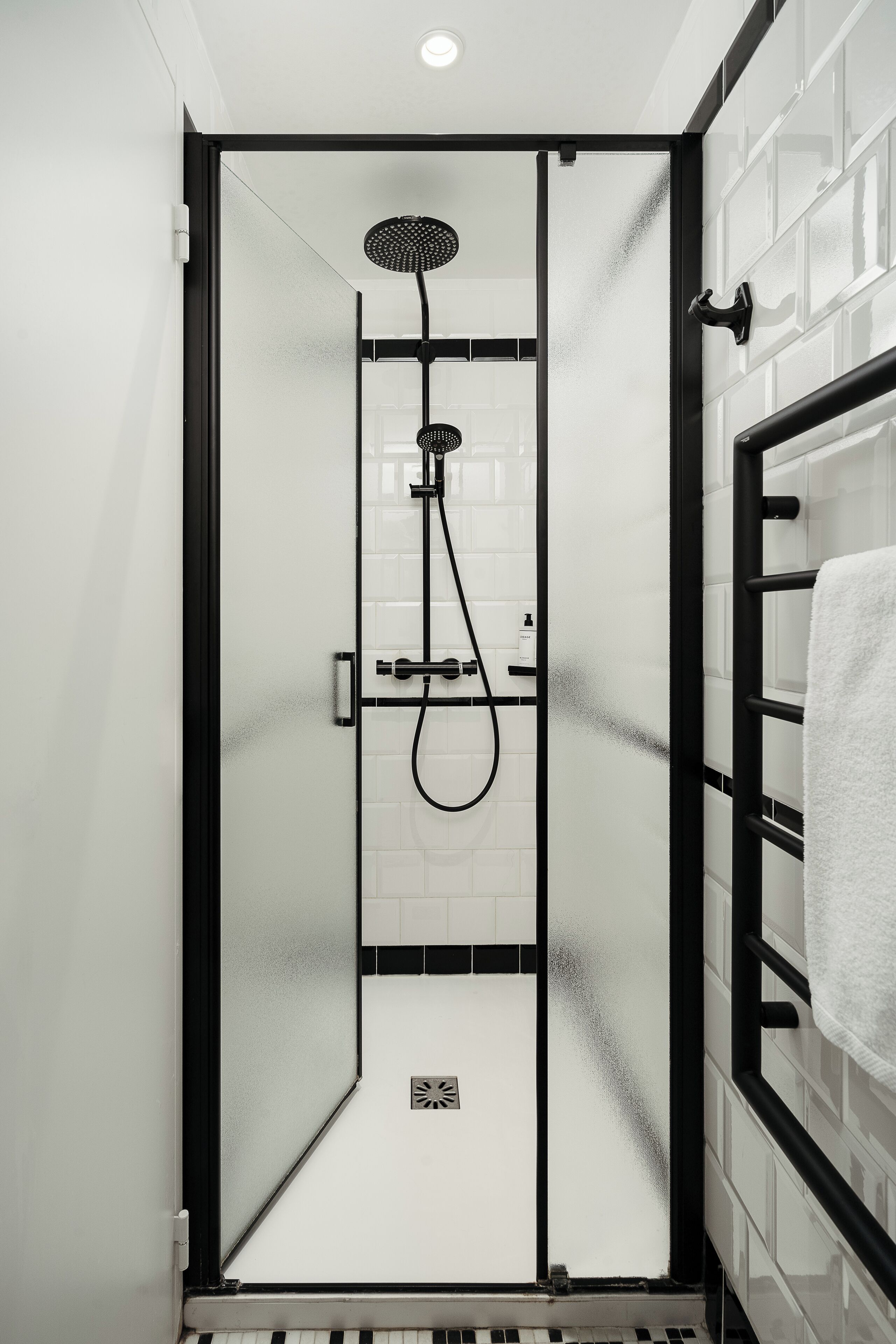 Una ducha moderna con puerta de cristal, marco negro y pared de azulejos blancos.
