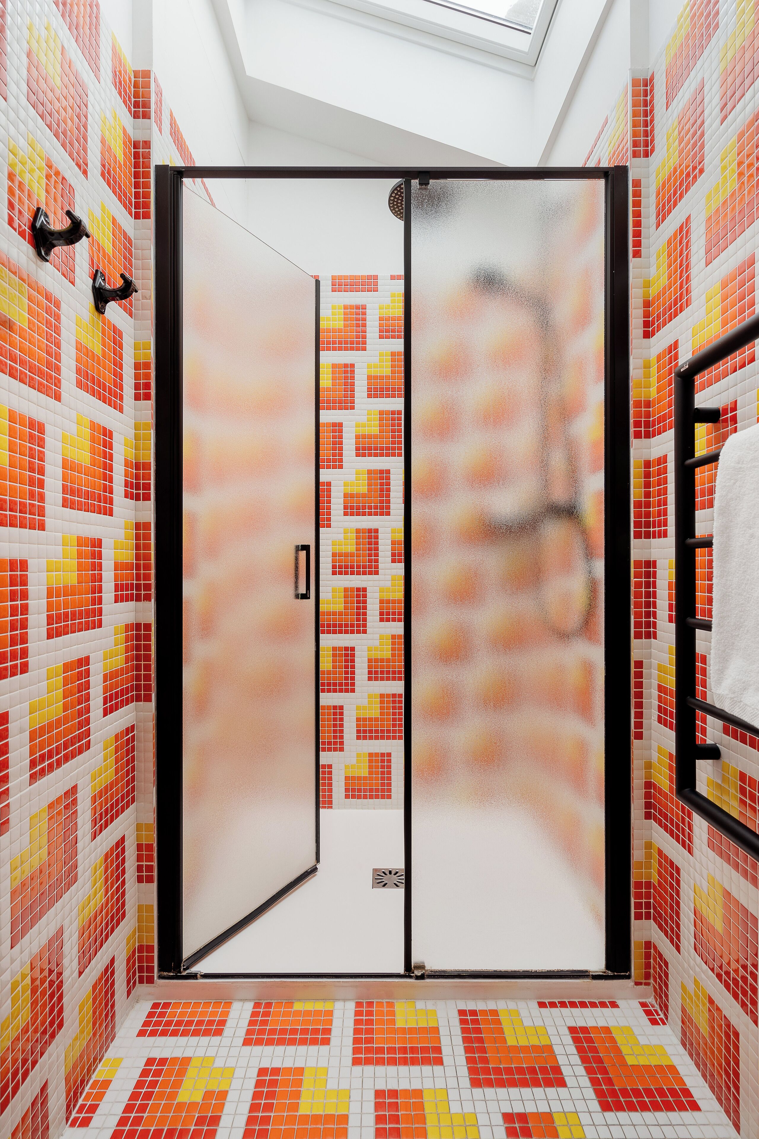 A bathroom with a tiled floor and walls, a frosted glass shower door, and a towel rack.