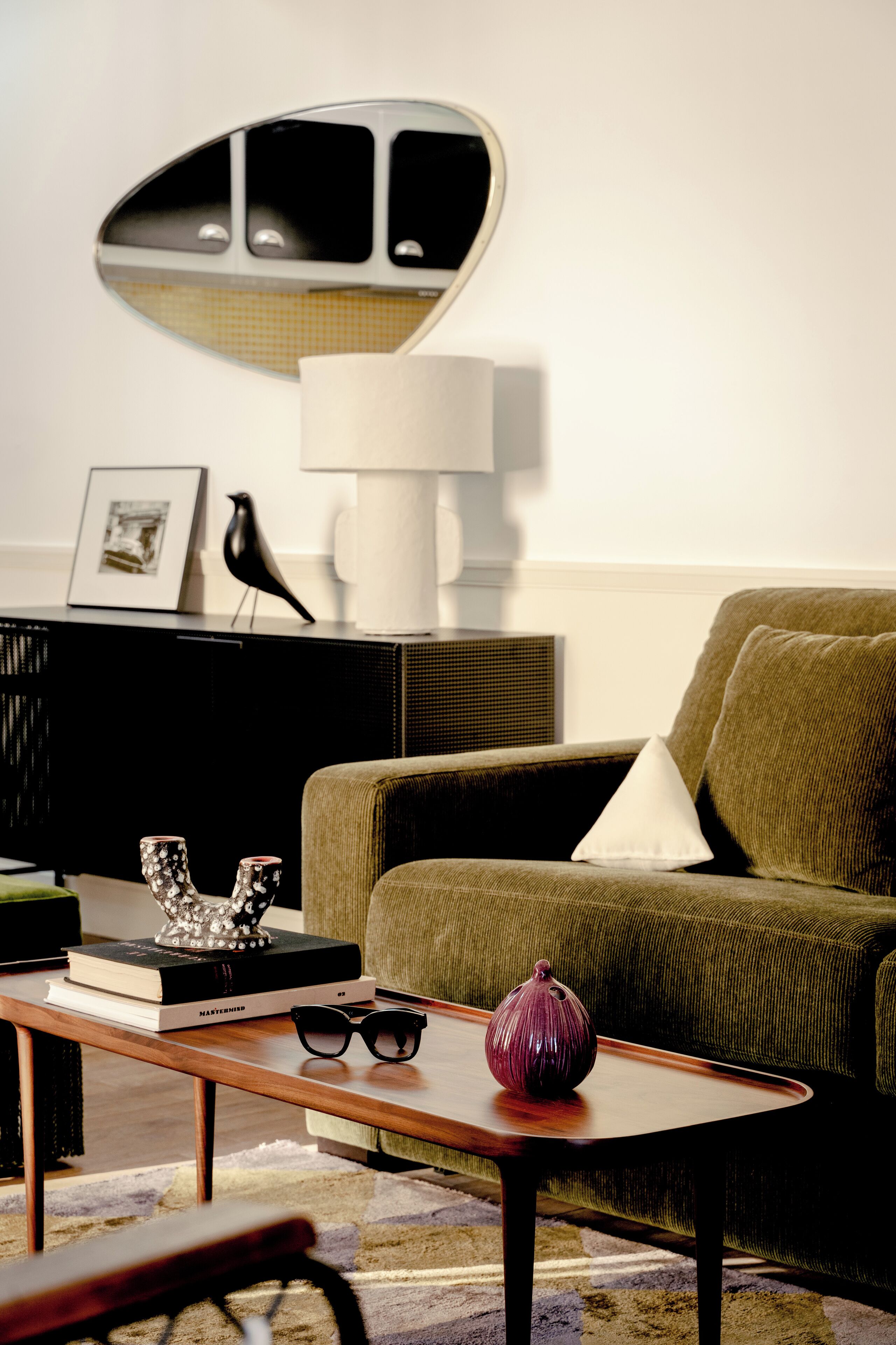 A living room with a green sofa, a wooden coffee table, a lamp, a framed picture, and a decorative bird statue.