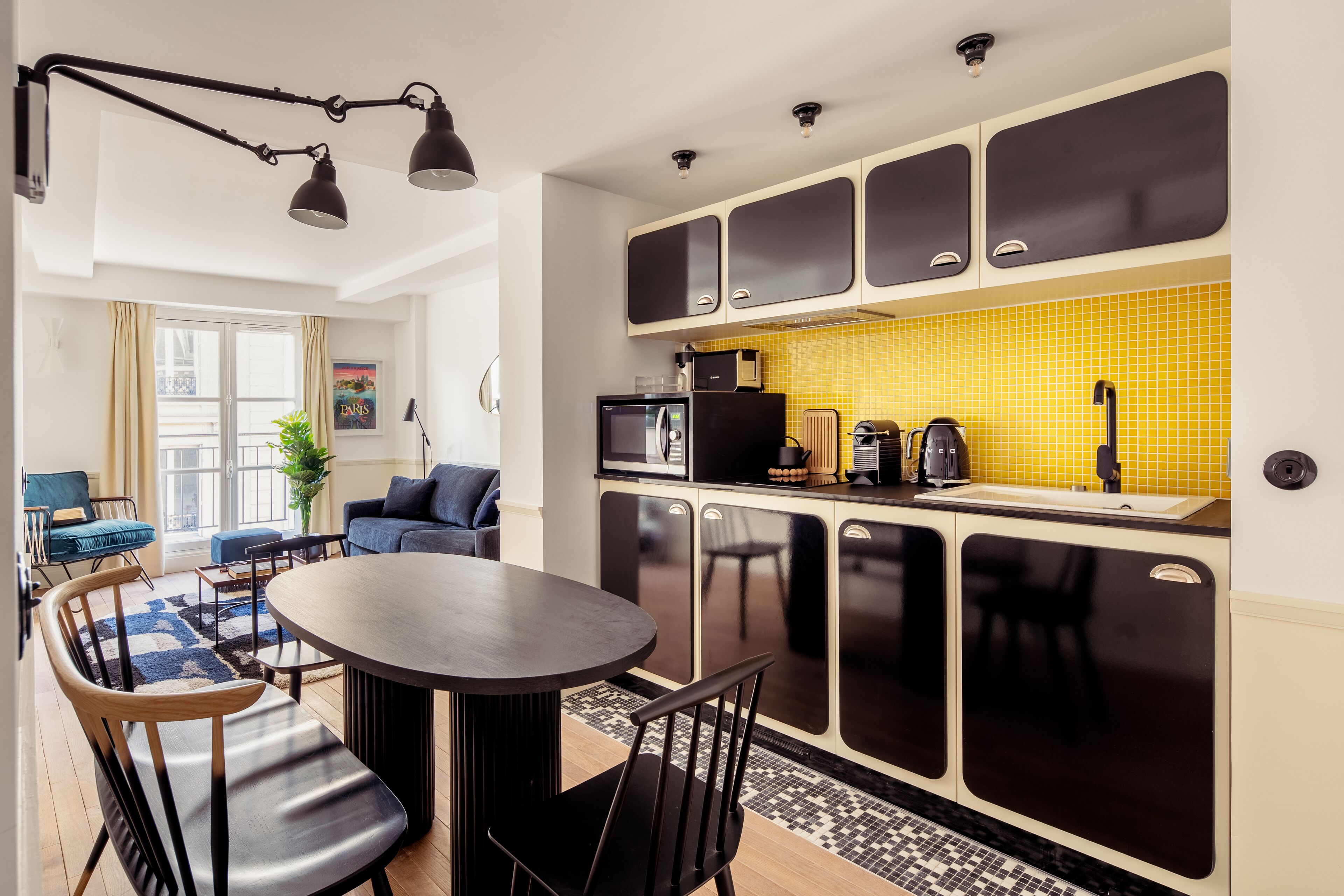 Une cuisine moderne avec des meubles de couleur noire, un pare-feu jaune et un coin repas comprenant une table ronde et des chaises.