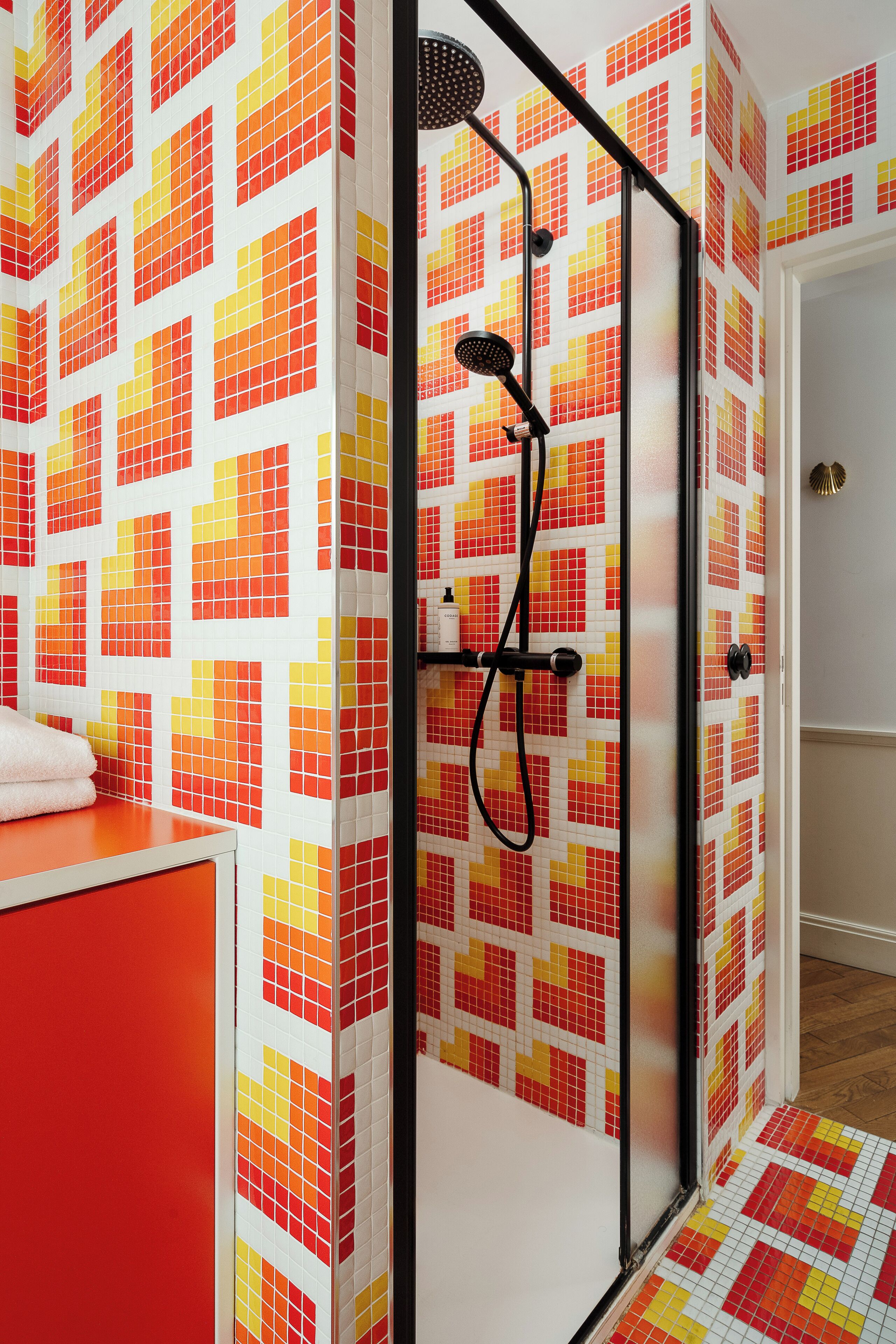 A shower enclosure with a tiled wall featuring a red and yellow pattern.