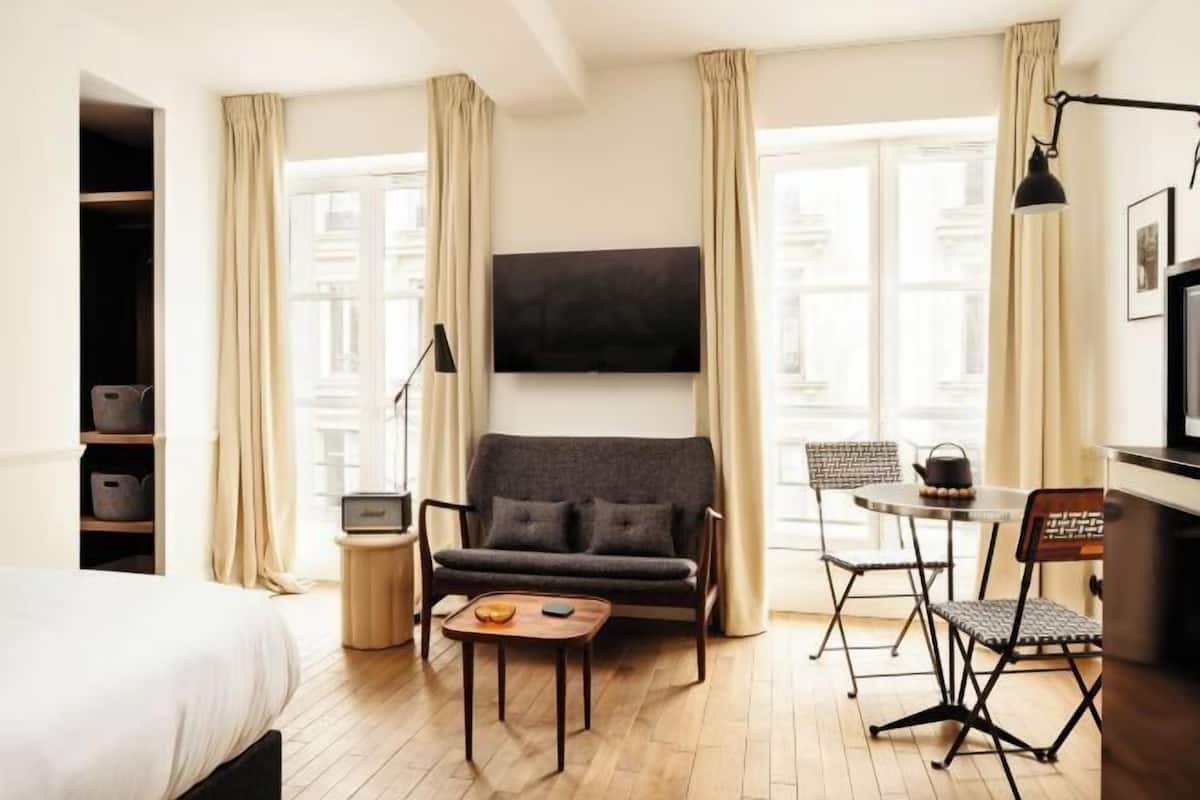 Ein Hotelzimmer mit Bett, einer Couch, einem kleinen Tisch, einem Fernseher und einem Essbereich mit Stühlen.