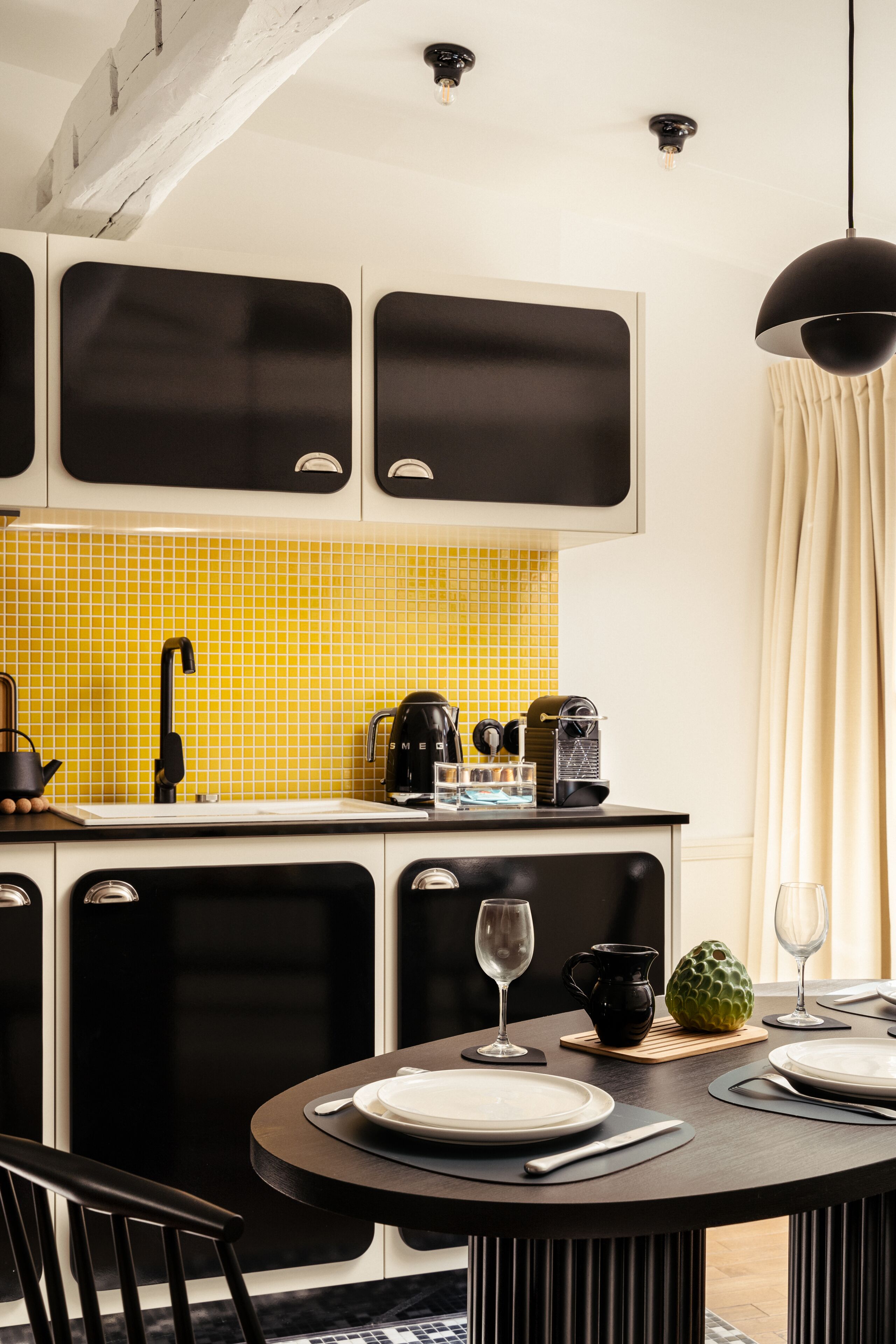 A modern kitchen with a yellow-tiled backsplash, black cabinets, and a dining area with a round table set for two.