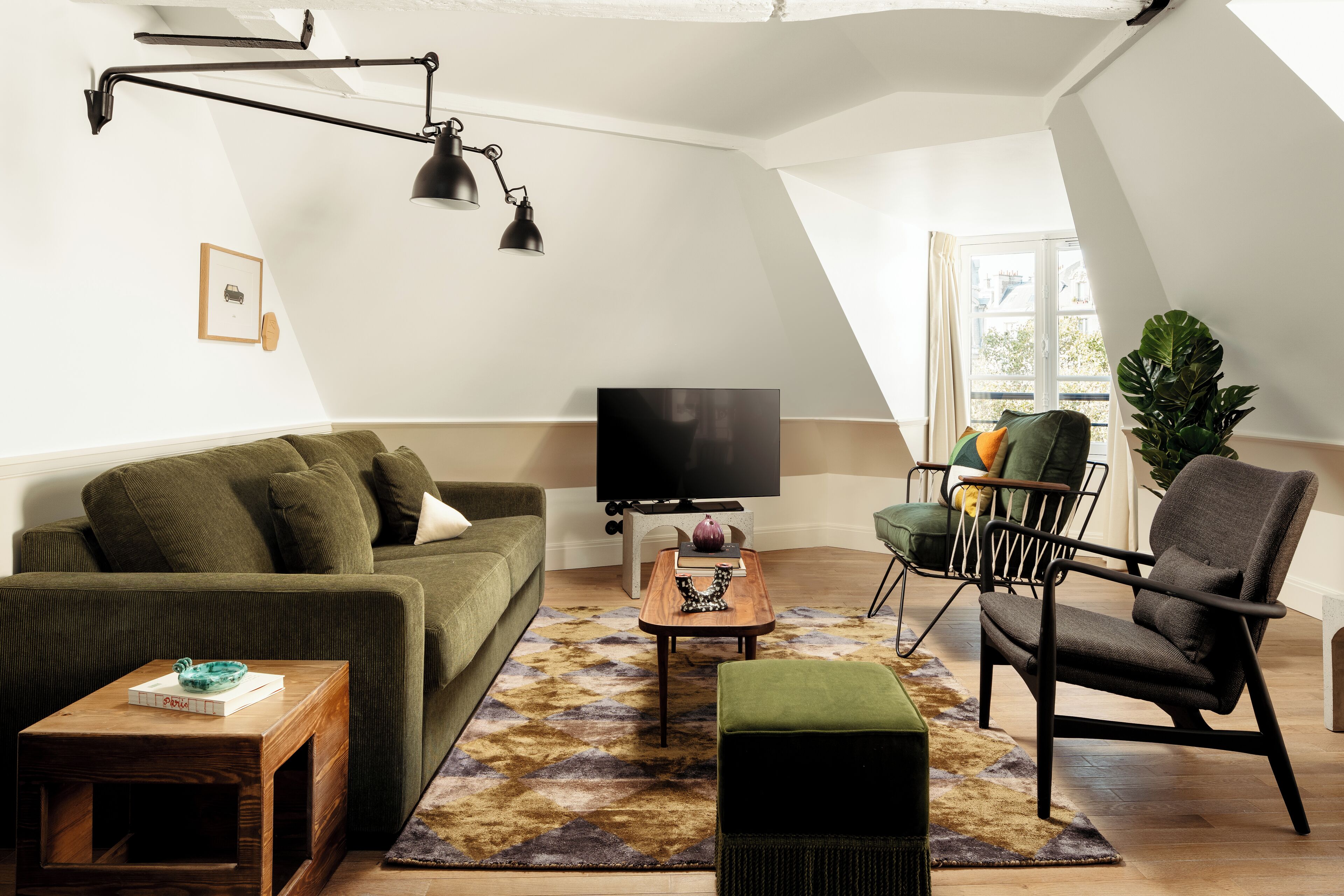 A modern living room with a green sofa, a wooden coffee table, a black armchair, and a TV on a white wall.