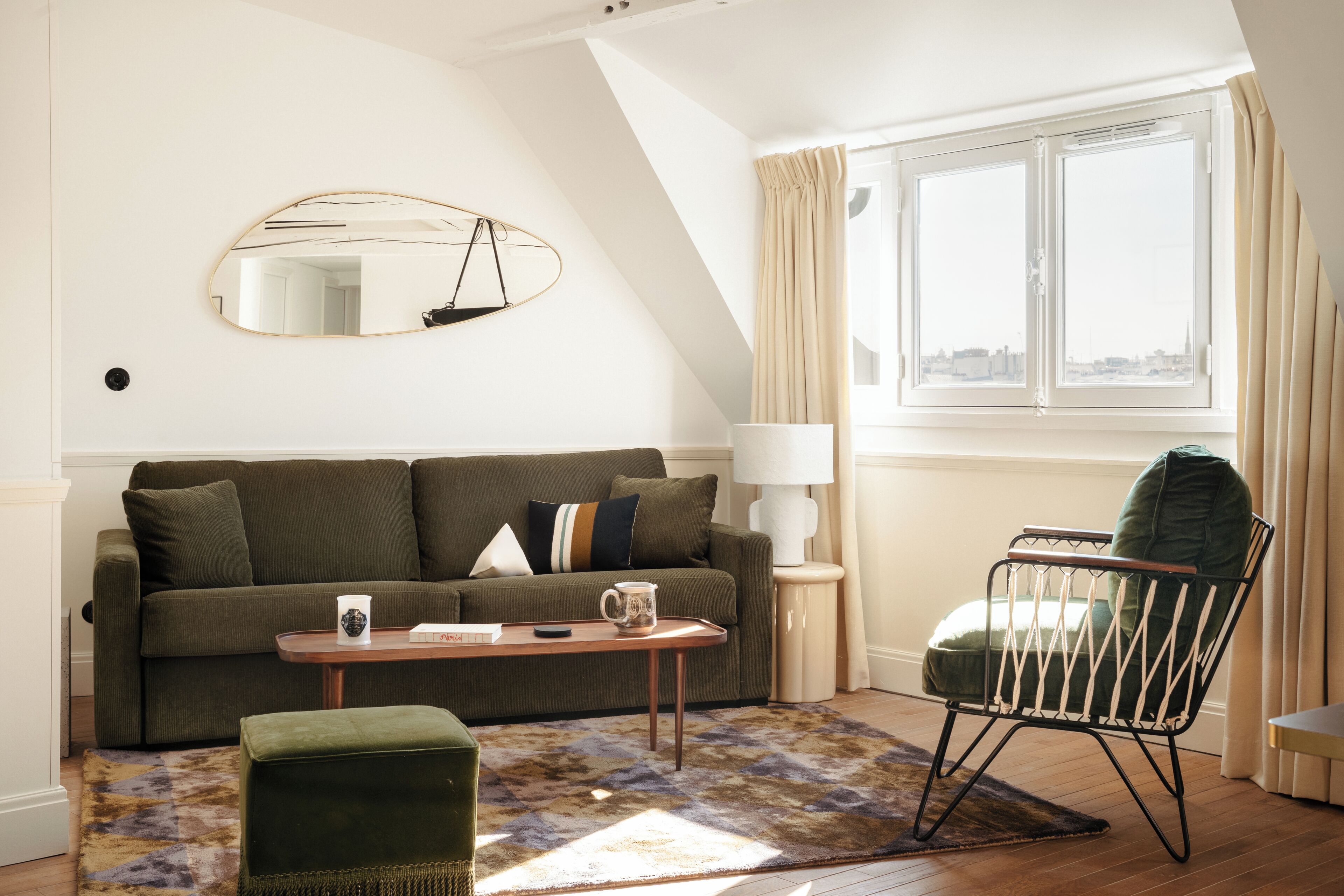 A cozy living room with a sofa, a coffee table, a chair, a mirror, and a window with curtains.