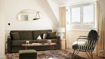 A cozy living room with a sofa, a coffee table, a chair, a mirror, and a window with curtains.