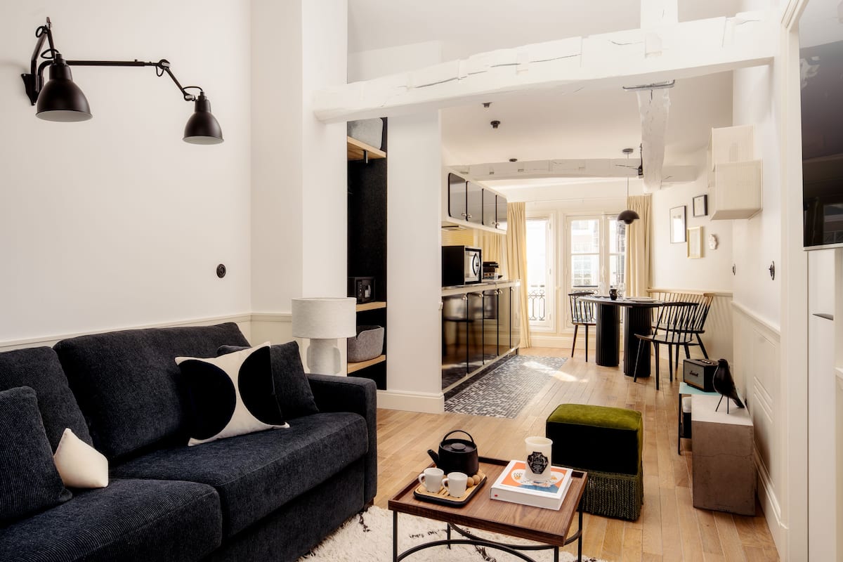 Ein modernes Wohnzimmer mit einem dunklen Sofa, einem Couchtisch mit einer Tablettauslage und einer Küchenzeile im Hintergrund.