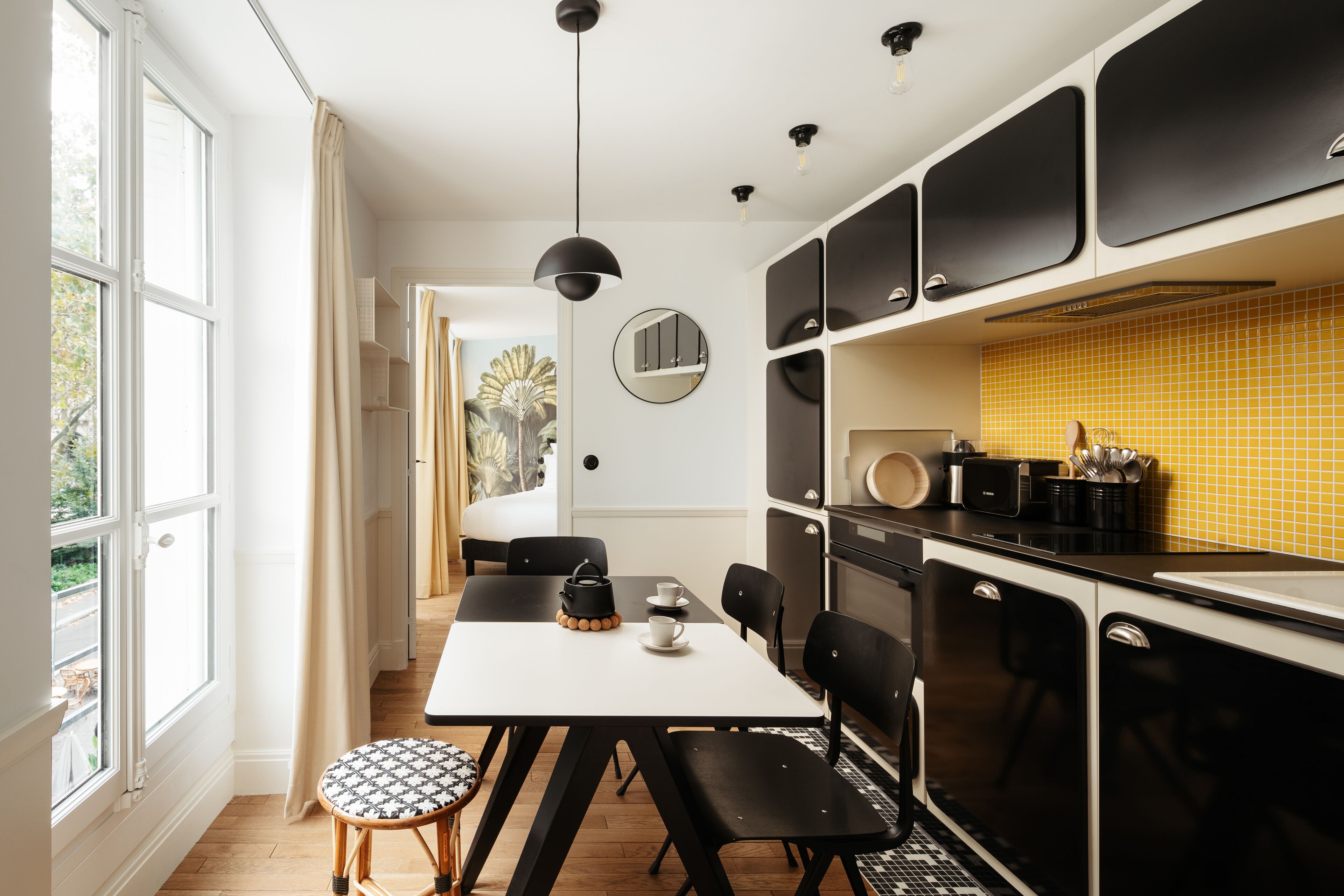 Una cocina moderna con armarios negros, un salpicadero amarillo y un comedor con una mesa blanca y sillas negras.