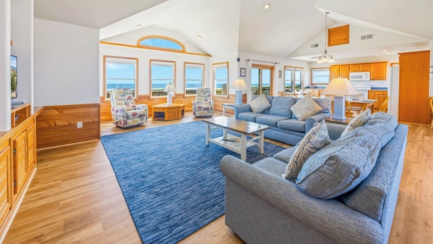 A spacious living area with a large sofa, a coffee table, and a view of the ocean through large windows. - Oceanfront Dog Friendly Home in Avon w/ Elevator, Hot Tub, Game Room, Wet Bar (Avon)