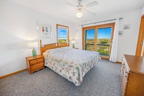 A bedroom with a bed, nightstands, a dresser, a ceiling fan, and a balcony with a view of the beach. - Oceanfront Dog Friendly Home in Avon w/ Elevator, Hot Tub, Game Room, Wet Bar (Avon)