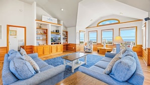A spacious living room with a large sofa set, wooden cabinets, and a television. - Oceanfront Dog Friendly Home in Avon w/ Elevator, Hot Tub, Game Room, Wet Bar (Avon)