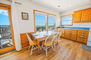 A dining area with a table and chairs, large windows with ocean views, wooden cabinets, and a view of the beach. - Oceanfront Dog Friendly Home in Avon w/ Elevator, Hot Tub, Game Room, Wet Bar (Avon)