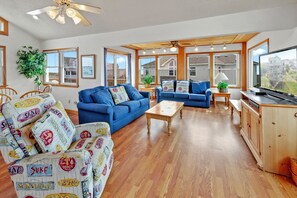 A spacious living room with blue sofas, a wooden coffee table, and a TV on a wooden cabinet.