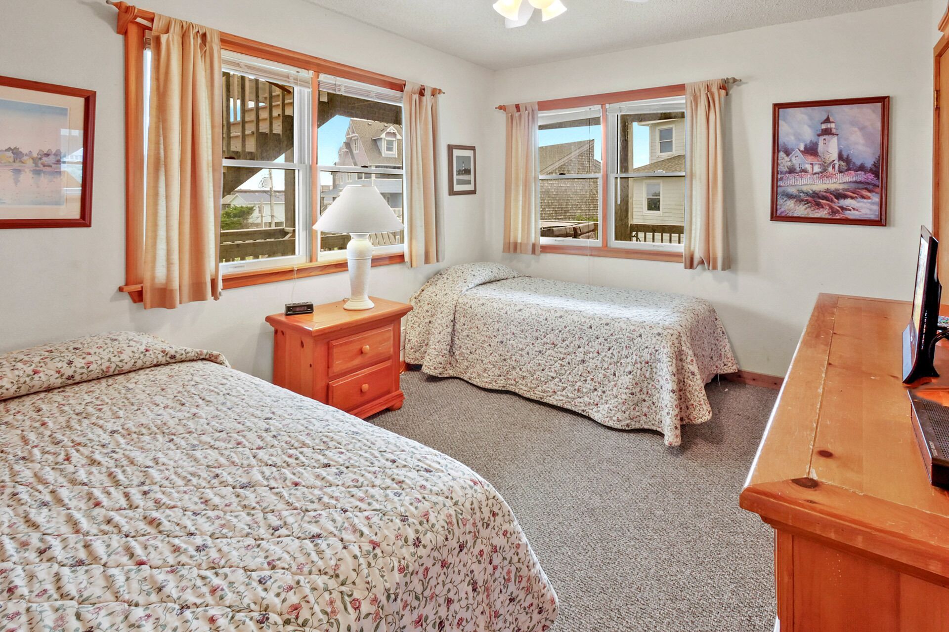 A bedroom with two beds, a nightstand, a lamp, and a wooden desk.