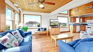 Amplia sala de estar con techo de madera, televisor y cocina con armarios de madera.