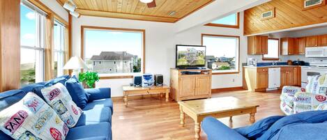 A spacious living area with a wooden ceiling, a television, and a kitchen with wooden cabinets.