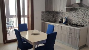A modern kitchen with a gas stove, a dining table with chairs, and a view through a glass door to an outdoor area. - Cozy Syracuse House (Siracusa)