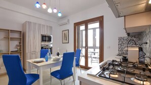 A modern kitchen with a gas stove, a microwave, and a dining area with blue chairs. - Cozy Syracuse House (Siracusa)