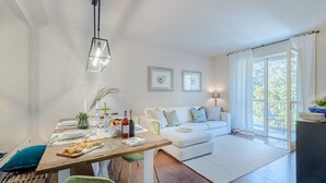 A modern living room with a wooden dining table, green chairs, a white sofa, and a large window with curtains. - A Seaside Sanctuary in the Heart of Viareggio (Viareggio)
