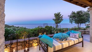 A cozy outdoor seating area with a view of the sea, stone walls, and candles.