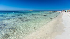 A beach with clear shallow waters, a sandy shore, and a distant island.