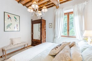 Un dormitorio con una cama grande, un banco de madera, un espejo y una ventana con cortinas.