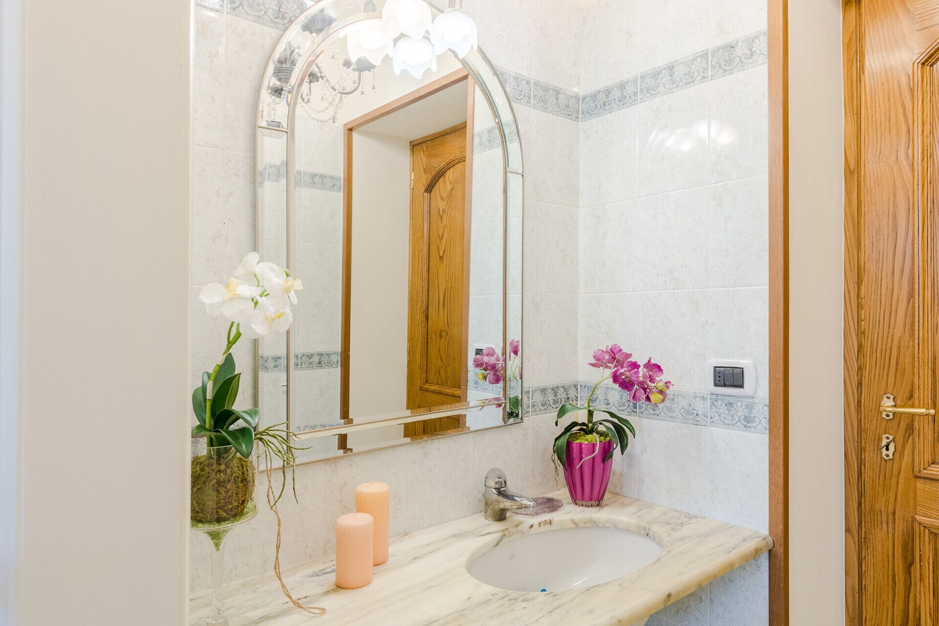 A bathroom with a marble sink, a wooden door, and a mirror with a chandelier.