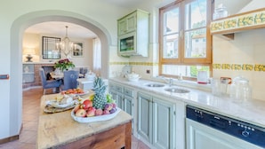A kitchen with a central island, a dining area with a chandelier, and a view of the outside through a window. - Nonna Bianca, a Genuine Farmhouse in Sant'Alessio, Lucca (Lucca)