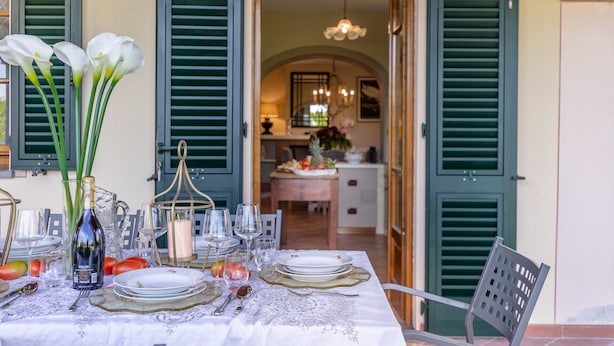 A dining table set with plates, glasses, and a bottle, with a view of a kitchen and dining area in the background. - Nonna Bianca, a Genuine Farmhouse in Sant'Alessio, Lucca (Lucca)
