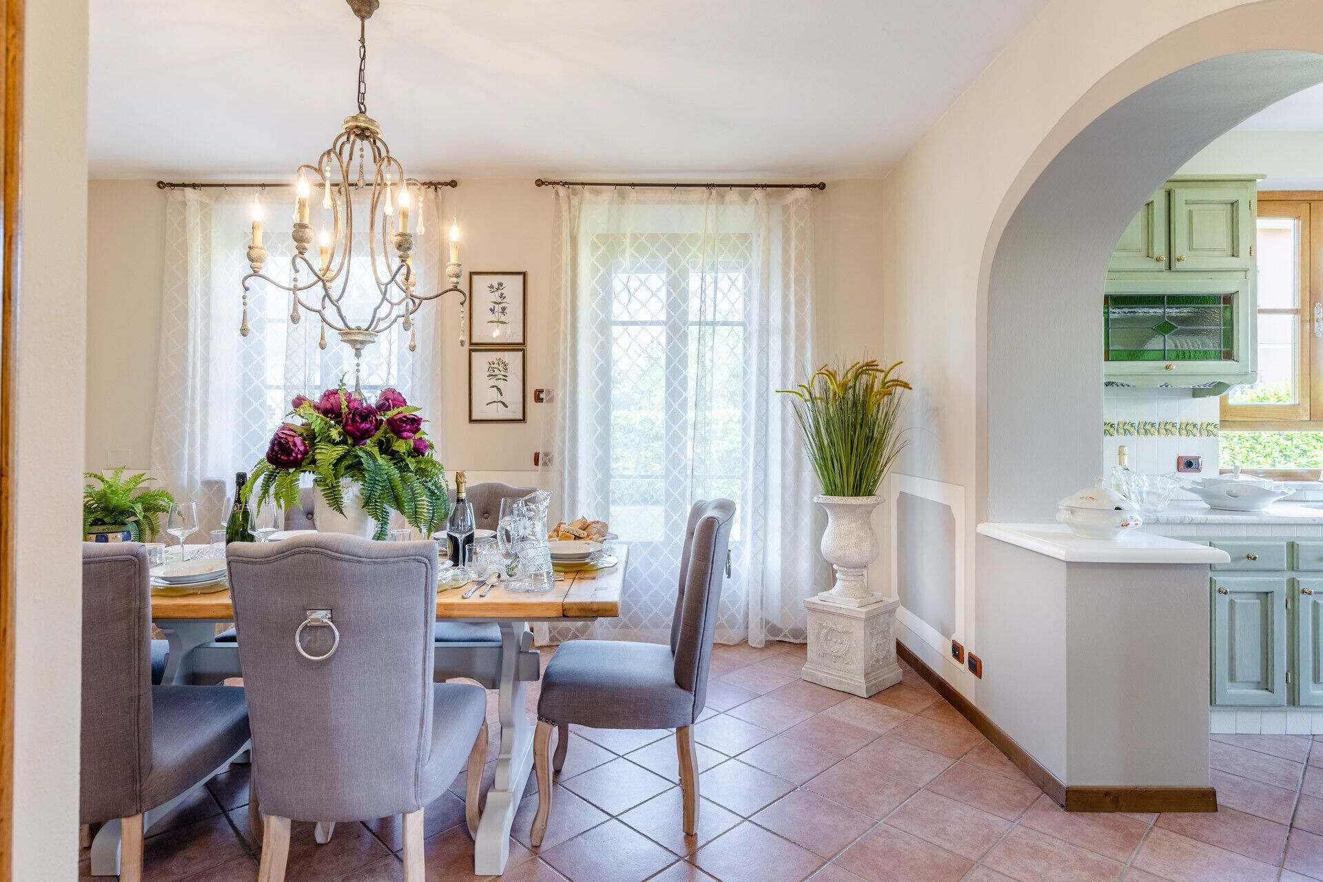 Un comedor con candelabro, una mesa preparada para cuatro personas y vista a la cocina a través de un arco.
