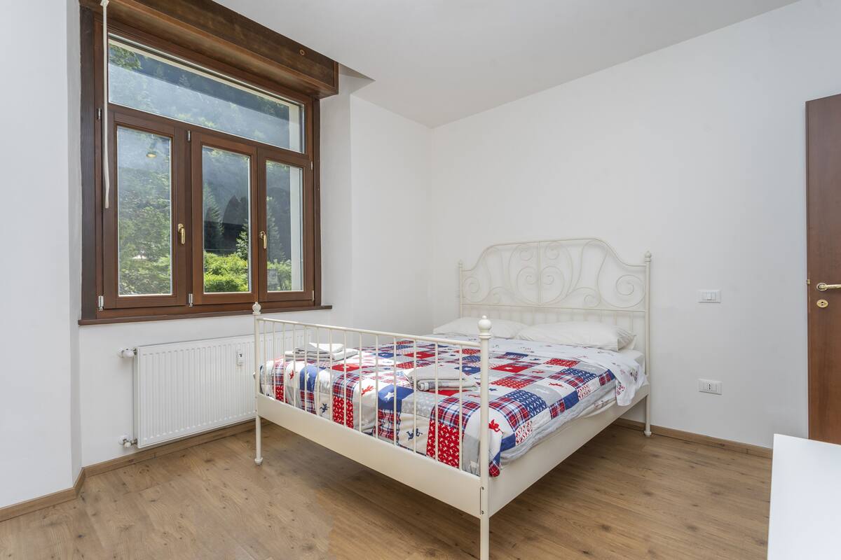 A bedroom with a white metal bed, a window with wooden frames, and a radiator.