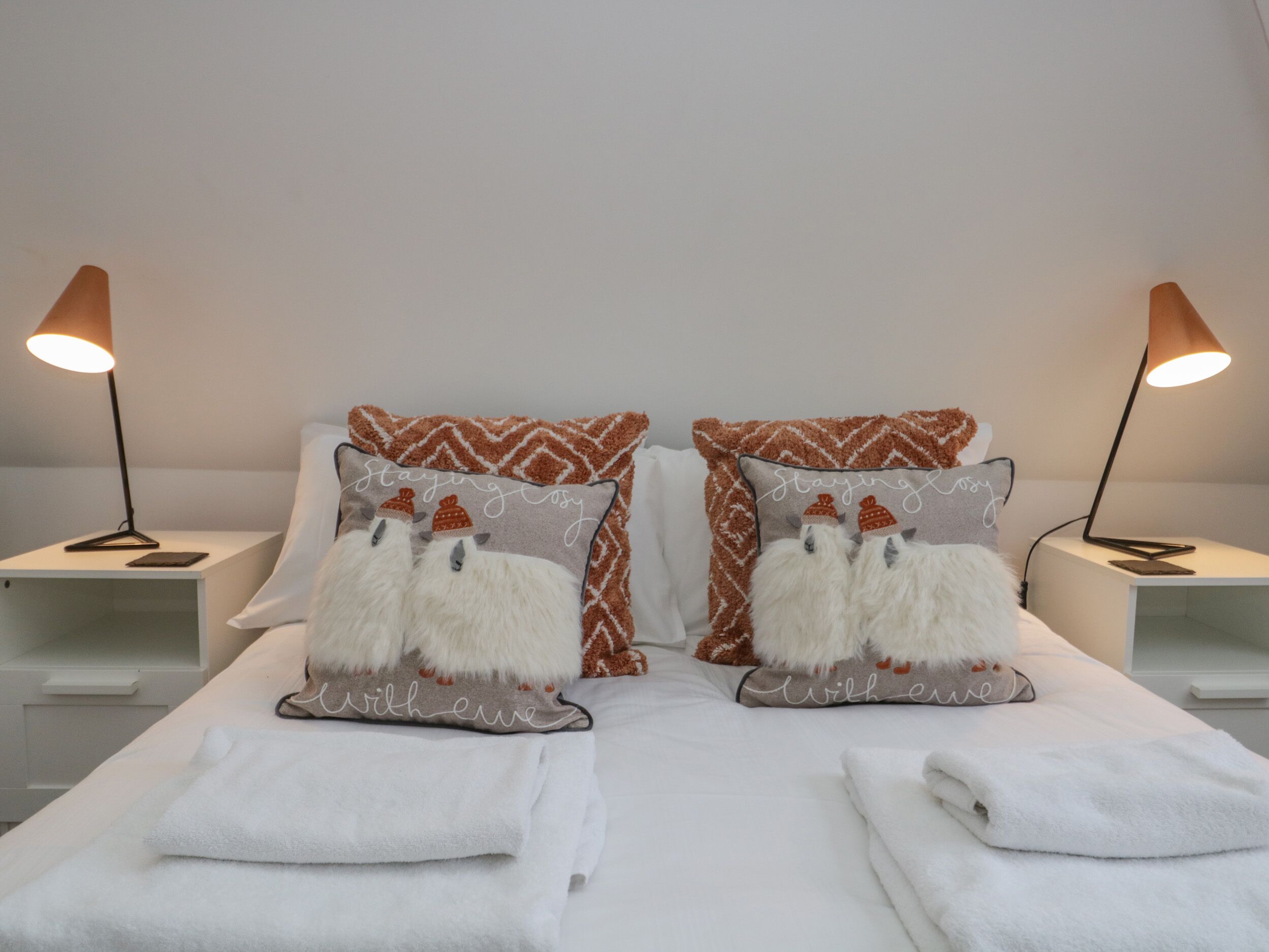 A neatly made bed with two pillows, two bedside lamps, and a pair of folded towels.