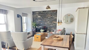 A modern living room with a stone wall, a wooden dining table, and a comfortable seating area. - Moorhurst Cottage (Grange-over-Sands)