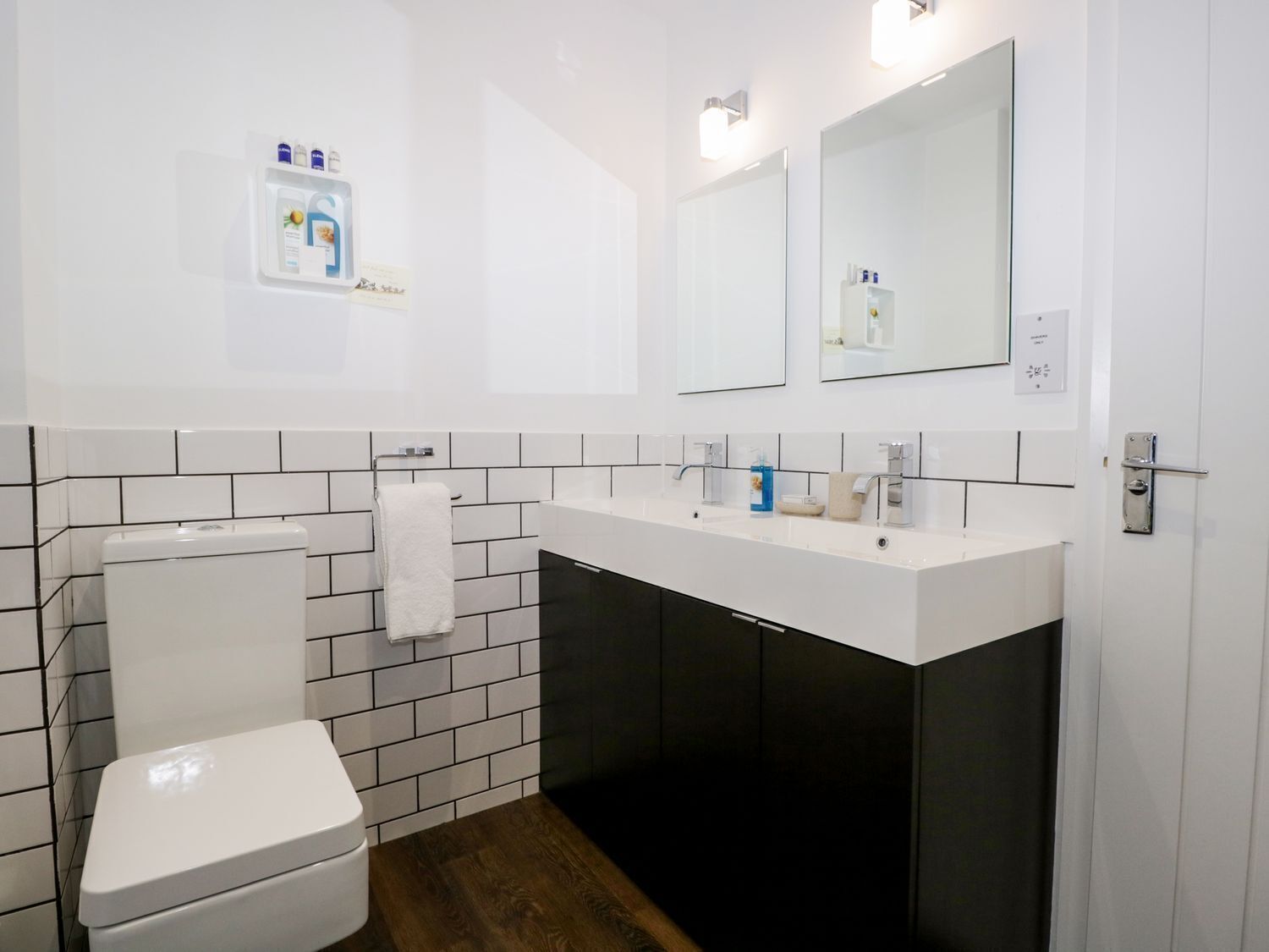 Une salle de bain moderne avec des toilettes blanches, un meuble-lavabo noir et un grand miroir au-dessus du meuble-lavabo.