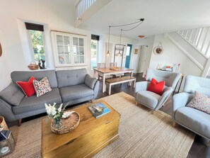 A modern living room with a grey sofa, a wooden coffee table, and a dining area with a wooden table and chairs.