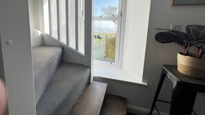 A modern interior with a staircase leading to a balcony, a potted plant, and a framed picture on the wall. - Moorhurst Cottage (Grange-over-Sands)
