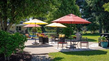Een terras buiten met meerdere parasols, rieten meubels en een pad van stenen.