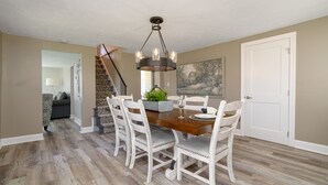 A dining area with a wooden table, white upholstered chairs, a chandelier, and a staircase leading to another room. - "Your Last-Minute Summer Escape-Pool, Waterfall, River Trails, Firepit & Horses" (Hinckley)