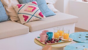 Un espacio de sala acogedor con un sofá, una bandeja con bebidas y cerezas, y una mesa con una silla azul.