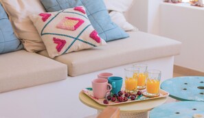 A cozy living area with a sofa, a tray with drinks and cherries, and a table with a blue chair.