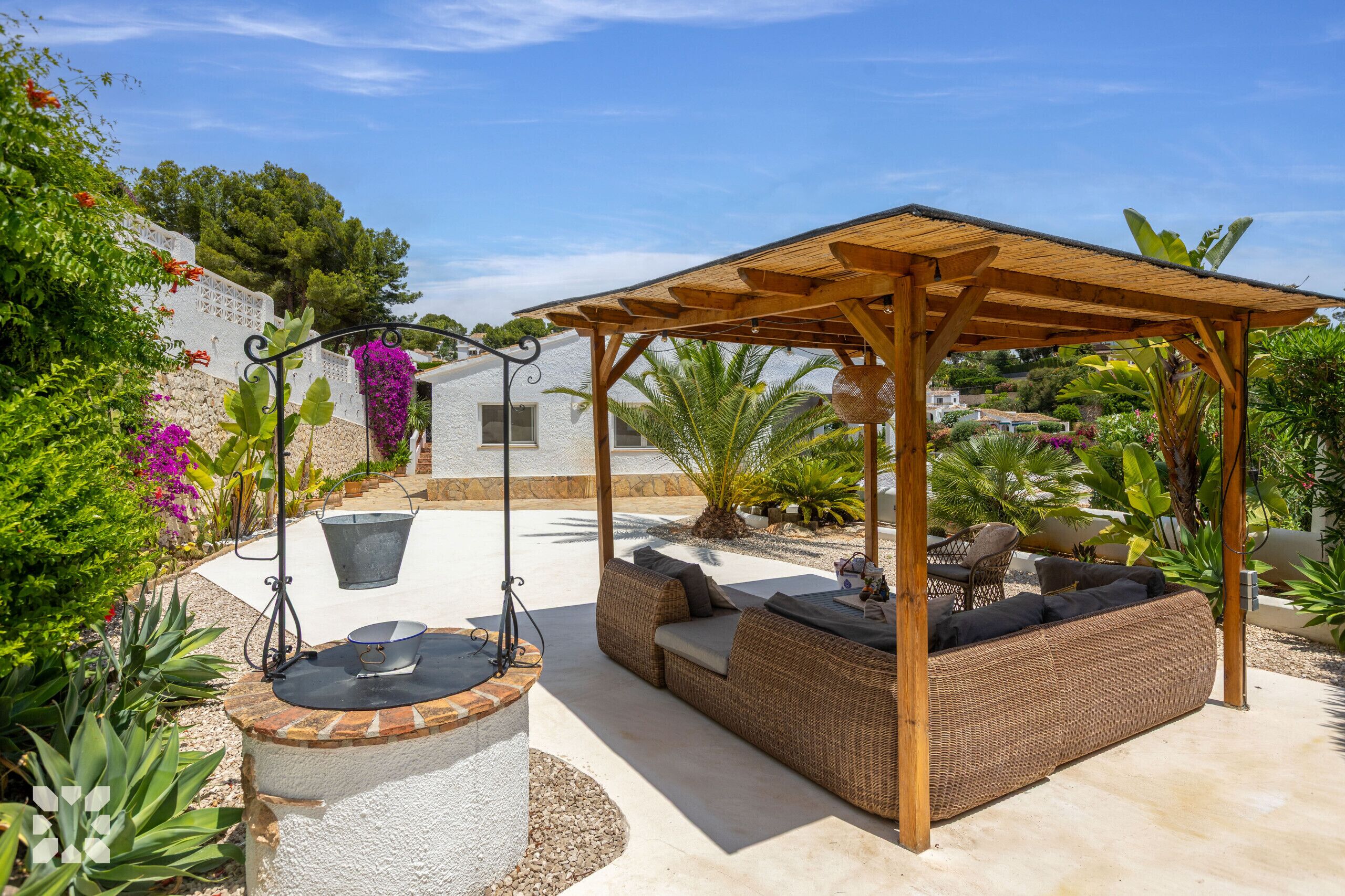 Un espace extérieur aménagé, abrité et doté de sièges, avec une balançoire, un foyer et un jardin où poussent différentes espèces de plantes.