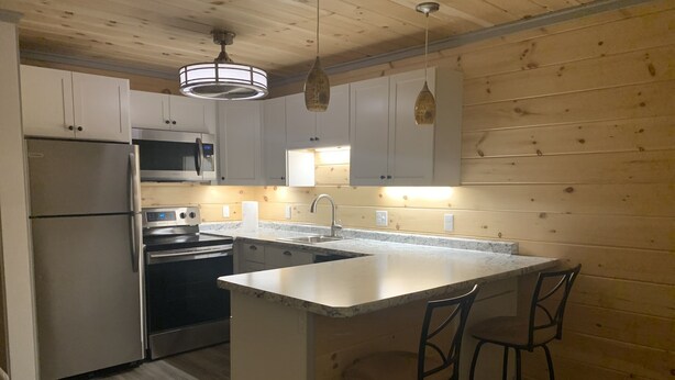 A modern kitchen with white cabinets, stainless steel appliances, a central island with bar stools, and wooden walls. - Simple and private (Boothbay)