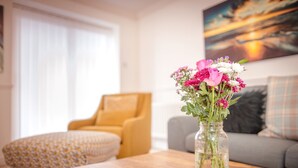 A living room with a wooden coffee table, a vase with flowers, a sofa, and a painting on the wall.