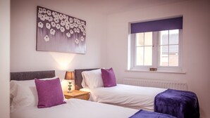A hotel room with two beds, a window with blinds, a radiator, and a wall-mounted painting.