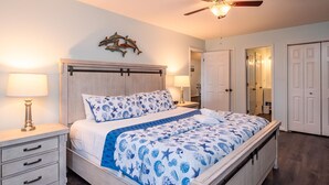 Ein Schlafzimmer mit einem Bett, Nachttischen, einem Deckenventilator und einer Wanddekoration.
