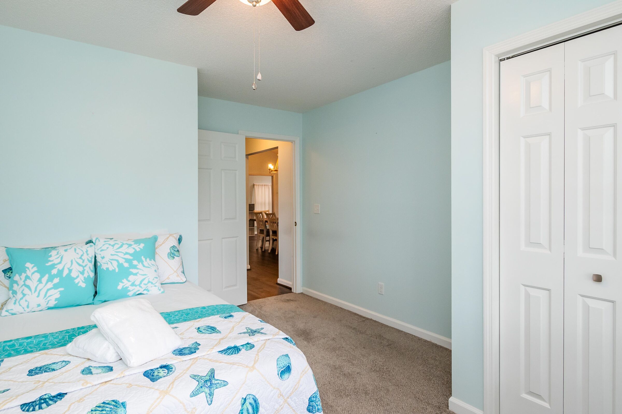 A bedroom with a bed, a ceiling fan, and a door leading to a hallway.
