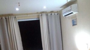 A hotel room with a bed, a chair, a nightstand, and a window with curtains.