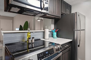 Una cocina moderna con un refrigerador de acero inoxidable, una estufa negra y una encimera blanca.